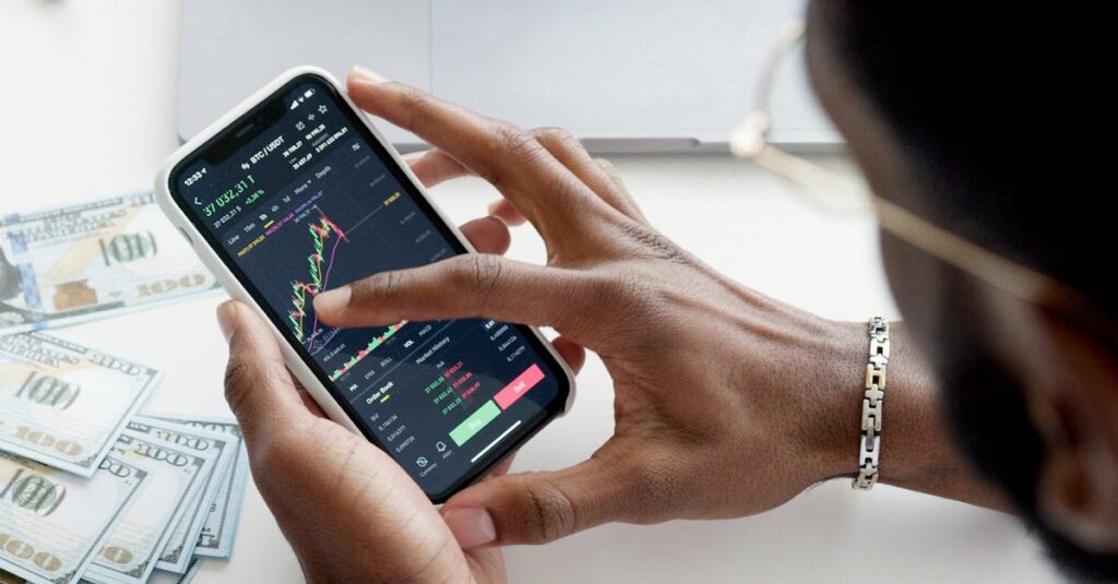 A person trading stocks using a smartphone, showcasing financial data on mobile and laptop screens.